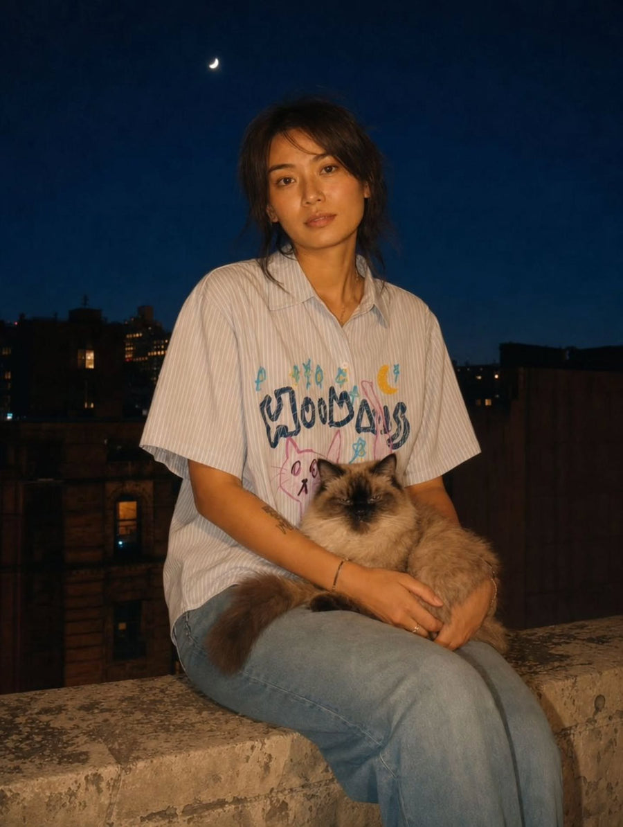 Woman in the Cat At Midnight striped boxy shirt on a rooftop at night with her cat on her lap
