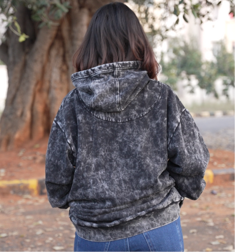 Person wearing a black acid-wash hoomans hoodie standing outdoors with a tree in the background