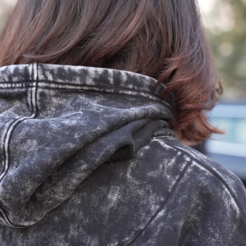 Person wearing an acid-wash hoodie with HOOMANS brand logo  with a blurred background