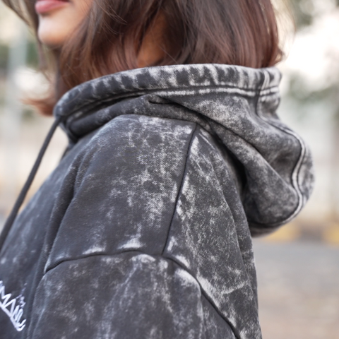 Person wearing an acid-wash hoodie with HOOMANS brand logo  with a blurred background