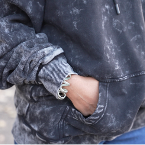 Person wearing an acid-wash hoodie with HOOMANS brand logo  with a blurred background