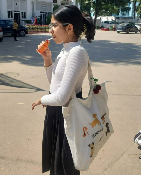 Girl drinking from a bottle with a tote bag featuring illustrations of dogs a street. Tote bag for dog moms.