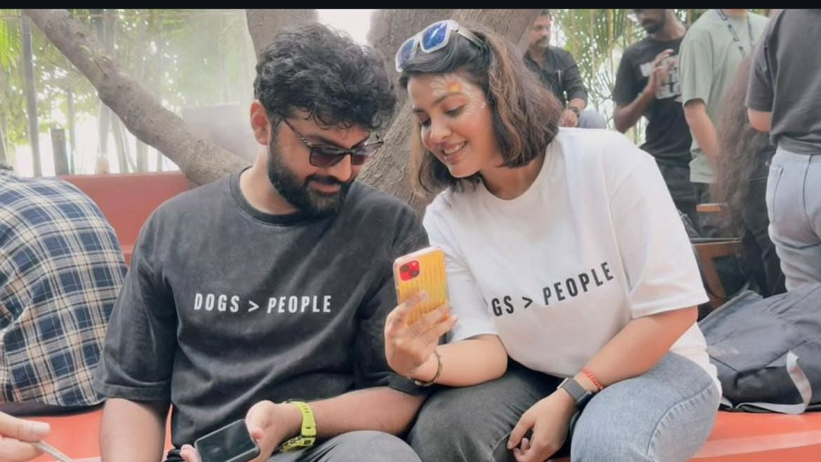 Two people sitting on a bench with dogs, one person holding a phone.