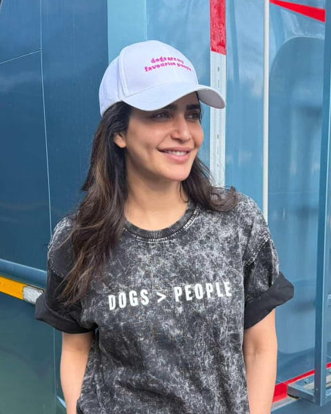 Karishma Tanna, wearing a cap and t-shirt with 'DOGS > PEOPLE' text, standing in front of a large vehicle.