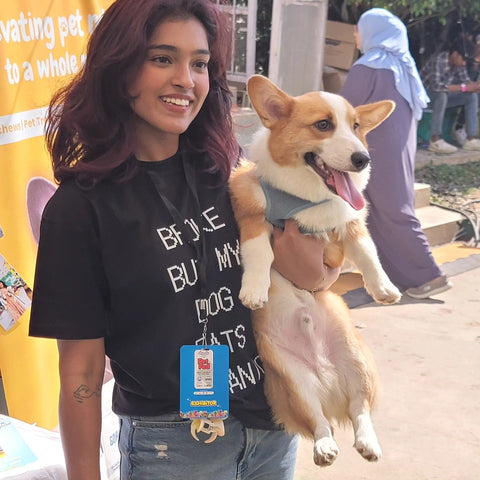 Real customer wearing the Broke But My Dog Eats Organic black tee holding her corgi at PetFed, Hoomans India