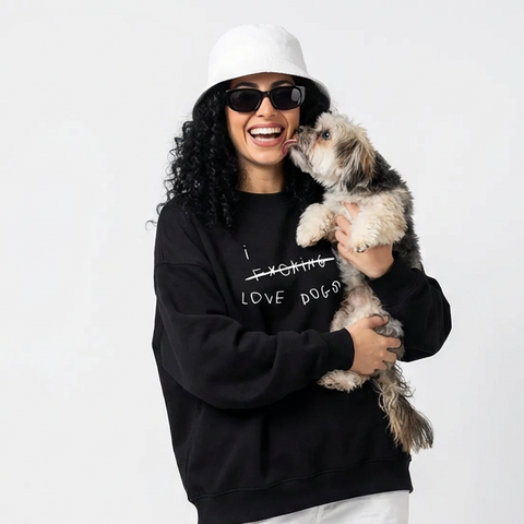 Person wearing a black hoomans sweatshirt with text, white pants, and sunglasses holding a small dog on a white background