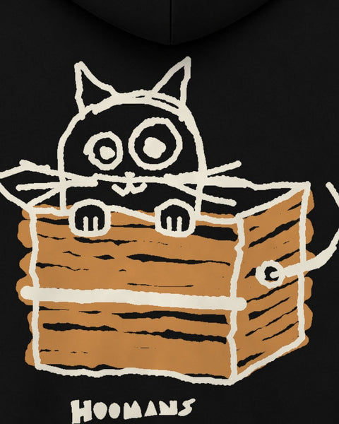 Close up of the back: a wide-eyed black cat peeking over the edge of a brown cardboard box