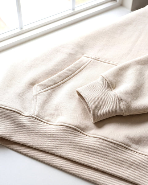 Kangaroo pocket edge, ribbed hem and ribbed cuff of the cream boxy hoodie