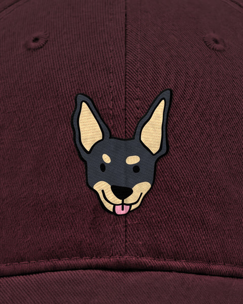 Embroidered black indie dog face in satin stitch on a maroon baseball cap, close up