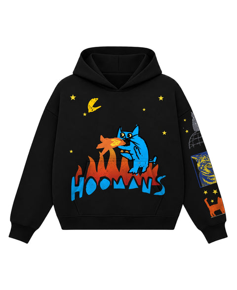 Black boxy hoodie with a blue cartoon cat breathing fire on a burning blue HOOMANS wordmark under a yellow moon and stars, front flat lay
