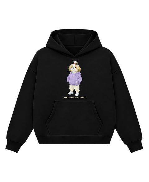 Black boxy hoodie with a painted shih tzu in a lavender hoodie and a red topknot bow above the line 'i don't walk. i'm carried.', front flat lay