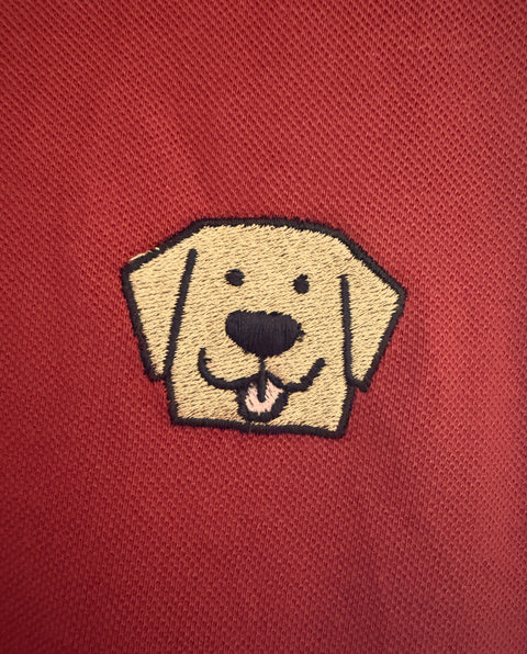 Close-up of the embroidered Labrador face on the Brick Red Lab Polo, tan and black thread on cotton piqué