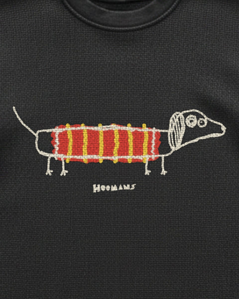 Close up of the long dog print on black waffle knit: a scribbly dachshund with stick legs and a striped jumper, the knit texture showing through the ink