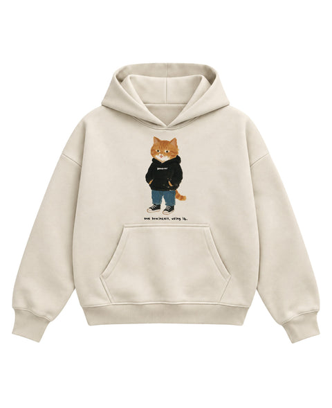 Cream boxy hoodie with a painted ginger tabby cat in a black hoodie, jeans and high-tops, tongue out, above the line 'one braincell. using it.', front flat lay
