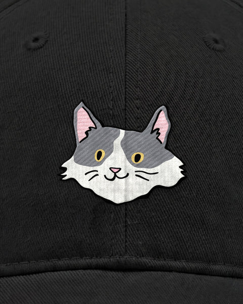 Embroidered white and grey cat face in satin stitch on a black baseball cap, close up